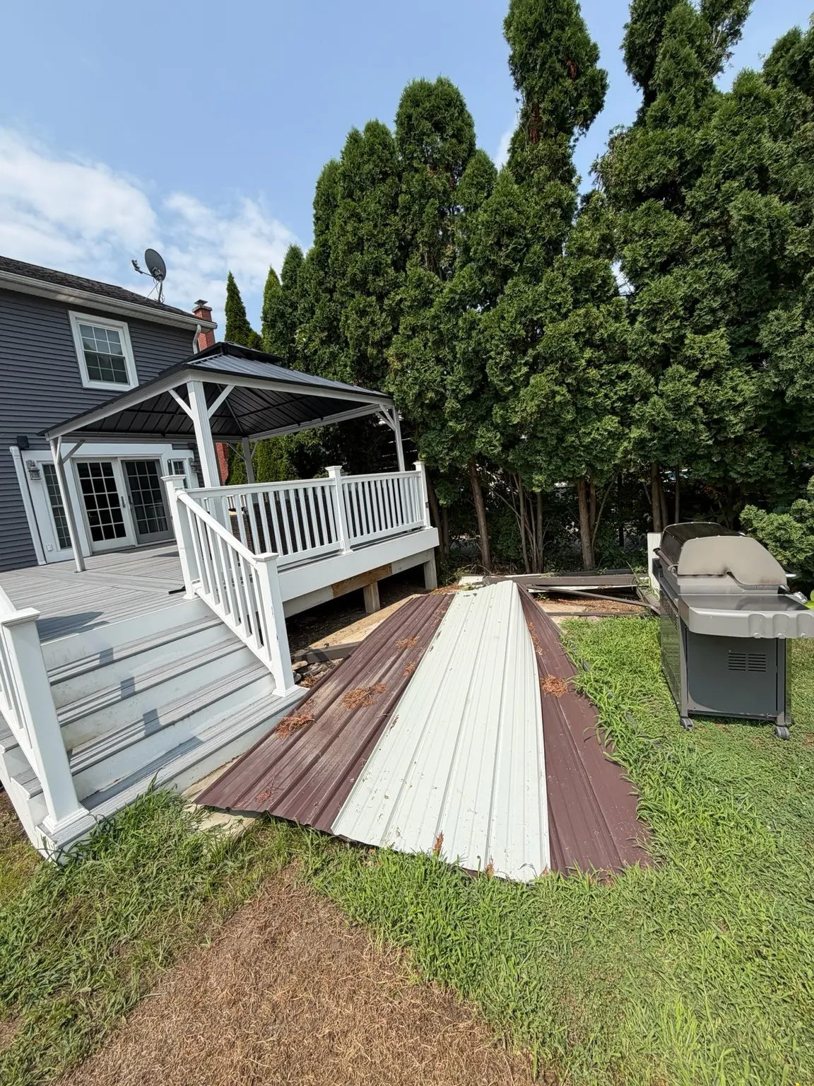 Dismantled metal gazebo panels and grill beside a backyard deck